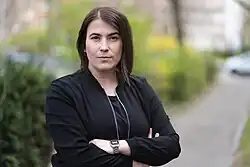 Im Vordergrund ist Natalie Cramme-Hill mit einer schwarzen Bomberjacke zu sehen. Der Hintergrund ist unscharf