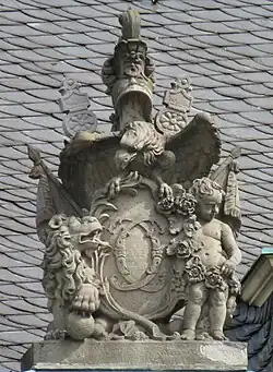 22. Trophäe – Liktorenbündel, Helm, Schwerter, Kugel, Adler, Löwe, Putto, Rosengirlande, Lanzenfahnen, Kartusche mit den Initialen CC von Herzog Carl Eugen.