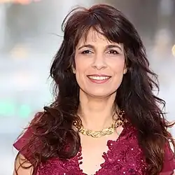 Darshan-Leitner hat langes braunes und leicht gewelltes Haar. Sie trägt ein rotes Oberteil und lächelt in die Kamera.