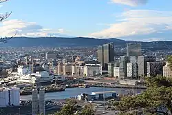 Foto einer Großstadt, die sich über fast das ganze Bild erstreckt. Im Vordergrund befinden sich in der Nähe einer Bucht mehrere Hochhäuser