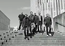 Schwarz-Weiß-Foto der 6-köpfigen Band PLEXIPHONES, die die Stufen des Museums Abteiberg hinuntergehen.