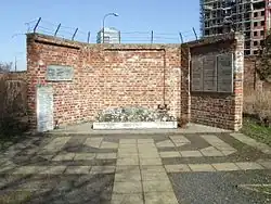 Mauer mit Steintafeln, am Fuß der Tafeln ein Blumenbeet