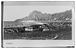historisches Foto eines Dorfes, im Hintergrund Berge und links das Meer