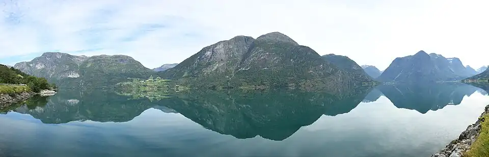 Panorama des Oppstrynsvatnet von der Südseite des Sees. Die Berge Oppigardshyrna und Lægdekulen sind in der Mitte des Bildes zu sehen. Links davon befindet sich der Ort Flo. Der Berg Hjellehyrna am Ostende des Sees ist rechts im Bild zu sehen. Links im Bild ist der Berg Marsåhyrna zu sehen