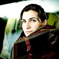 Pelin Esmer 2019. Junge türkische Frau mit durchdringendem Blick und einem hoch gewickelten Schal. Eine einzelne Haarsträne hängt ihr über die Schläfe.