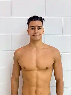 Secchi steht mit nacktem Oberkörper vor einer weißen Wand.