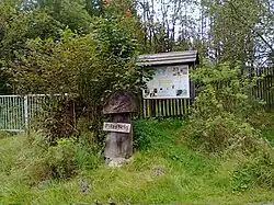 Das Logo des Pilzsteiges, ein hölzerner Pilz. Im Hintergrund eine Schautafel.