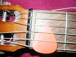 Verbreitete Methode, das Plektrum bei Nichtbenutzung an der Gitarre zu deponieren