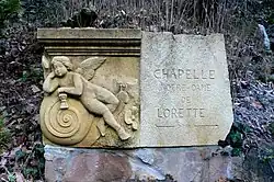 Wegweiser zur Lorettokapelle Murbach mit der Spolie «Genius auf einer Schnecke»