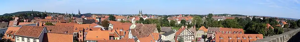 Panoramablick über Quedlinburg mit roten Ziegeldächern, Fachwerkhäusern und mehreren Kirchtürmen unter blauem Himmel
