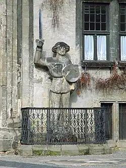 Steinerne Roland-Statue mit Schwert und Schild an einer Hauswand in Quedlinburg, umgeben von einem schmiedeeisernen Geländer