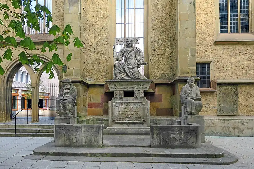 Das Reformationsdenkmal vor dem erhaltenen Rest der Südfassade, links das ehemalige Südportal der Kirche