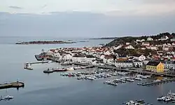 Foto einer Stadt mit vielen weißen Holzhäusern, die direkt an der Küste liegen. Nicht unweit davon befinden sich mehrere kleinere Inseln.