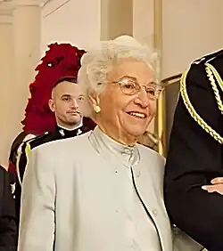 Colvin steht aufrecht eingehakt bei einem im Bildausschnitt nur teils zu sehenden Herren in schwarzer Uniform, lächelt und blickt rechts am Betrachter vorbei. Sie hat weißes Haar und trägt ein hellgraues Kleid mit einem farblich passenden Jackett. Im Hintergrund sind ein weiterer Mann in Uniform sowie festliche Dekoration und die weiße Inneneinrichtung des Weißen Hauses zu sehen.