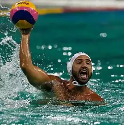 Felipe Perrone ist im Wasser und hält den Ball in seiner rechten Hand. Er trägt einen Vollbart und eine weiße Badekappe.