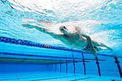 Alexander Graham in Aktion mit kurzer Badehose, weißer Badekappe und Schwimmbrille