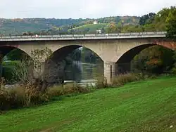 Steinerne Bogenbrücke, Eisenbahn oben, mittelgroßer Fluss (Saale) unten. Im Hintergrund ein Weinberg und Wald.