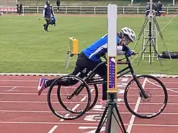 Frau mit Frame Runner sprintet über die Ziellinie, Zeitnahme-Geräte sind zu sehen