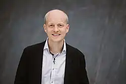 Sandro Kappe, zuversichtlich lächelnd vor einer grauen Wand in Hamburger Innenstadt