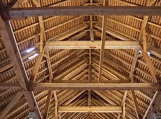 Großes Pfettendach: Der Dachstuhl ist als Binder (Dachbinder) ausgeführt, alle fünf Sparrenfelder ein Binder. Der Längsverband, aus Firstpfette und Mittelpfetten, ist mit Kopfbändern ausgesteift (Kopfbandpfetten). Die Hängepfosten mit angehängtem Binderbalken (Bundbalken) sind hier nicht weiter belastet. Die Bundbalken sind mit einer doppelten Brettreihe in Längsrichtung stabilisiert.