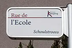 Zweisprachiges Schild in Käerjeng: Schoulstrooss (luxemburgisch) / Rue de l'École (franz. für Schulstraße)
