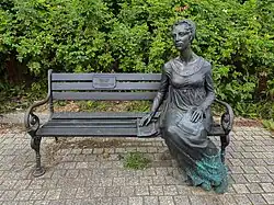 Skulptur in Form einer Bank, auf der Sophie Auguste Tilebein sitzt, neben sich ein Manuskript