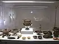 Im Vordergrund links ein aus Goldblech gefertigtes Diadem (daneben ein vom Museum in die Vitrine gestelltes Vergrößerungsglas)