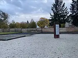 Das Fundament der ehemaligen Anstaltsscheune, im Hintergrund eine Mauer und Bäume.