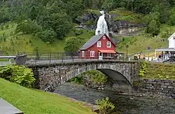 Foto einer steinernen Brücke über einen Fluss mit einem Wasserfall im Hintergrund