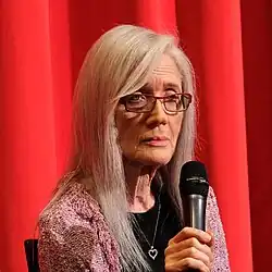 Porträt von Stephanie Rothman, konzentrierter Blick, vor rotem Kinovorhang mit Mikro in der Hand