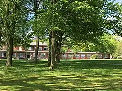 Eine große Grünfläche mit einem zweigeschossigen Rotklinkergebäude im Hintergrund