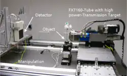 Eine Sub-Mikro-CT-Anlage. Rechts die Röhre, links der Detektor. Sehr nah an der Röhre und sehr klein das Prüfobjekt auf einer Nadelspitze auf einem Drehteller.