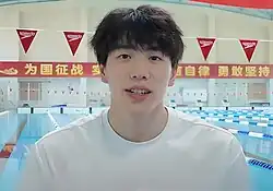 Sun Jiajun trägt ein weißes Hemd. Im Hintergrund ist ein Schwimmbecken und darüber sind chinesische Schriftzeichen.