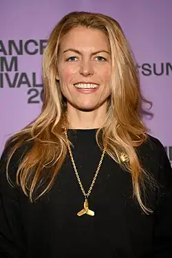 Ein Porträt der Regisseurin Susanne Regina Meurs aus dem Jahr 2020, das beim Sundance Film Festival aufgenommen wurde. Sie hat lange blonde Haare ohne Pony und trägt einen schwarzen Pullover. Darüber eine auffällige goldene Kette aus groben Kettengliedern, an der ein goldener Schiffspropeller hängt.