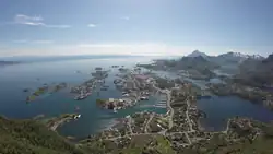 Foto von einer Anhöhe auf eine an der Küste gelegenen Stadt hinab. Im Hintergrund mehrere bergige Inseln