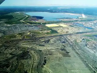 Links: Satellitenaufnahme des nördlichen Teils der „Millennium Mine“ der Suncor Energy und angeschlossene Infrastruktur. Der große Fluss in der linken Bildhälfte ist der Athabasca River. Rechts: Teil des Tagebaus sowie Schwefelhalden und Absetzbecken („Syncrude tailings pond“) der Aufbereitungsanlage „Mildred Lake“ von Syncrude.
