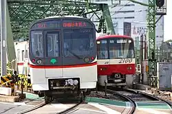 Tokio: Begegnung eines Zuges der Asakusa Line der Toei (links) und der Keikyū (rechts) an einem Bahnübergang im Netz der Keisei