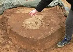 Halb freigelegte Urne im stehen gelassenen Erdsockel