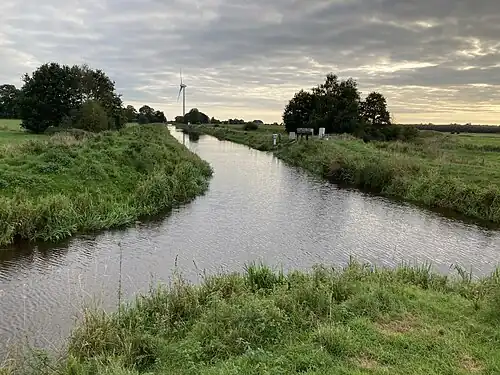 Ursprung des Sauteler Kanals am Zusammenfluss der Flumm (von links) und der Alten Flumm (von rechts). Der Sauteler Kanal erstreckt sich in Richtung der abgebildeten Windkraftanlage. Am rechten Ufer ist das Abschlagsbauwerk zu erkennen, durch das Wasser aus dem Kanal zur unteren Flumm abfließt, welche rechts von der rechten Baumgruppe verläuft.