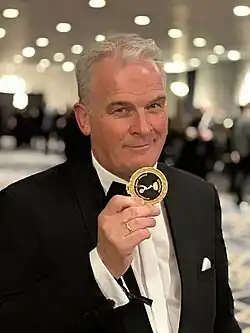 Volker Schmidt-Sondermann bei den International Emmy Awards in New York, 2023 (Nominierung „Triff... Anne Frank“). Volker Schmidt-Sondermann zeigt eine Nominierten-Medaille.