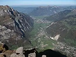 Ansicht von Süden; links Aufschwung zu Wiggis und Rautispitz. Orte: Rechts unten Glarus, links erst Riedern, dann Netstal, Mollis/Näfels und Niederurnen am Talausgang