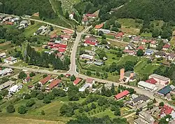 Luftbild eines Dorfes mit mehreren kleinen Straßen, an denen Häuser stehen. Umgeben ist die Siedlung von Wiesen und Bäumen.