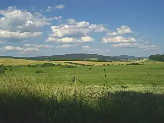 Klingeberg (677,2 m, Mitte) und Bleßberg (866,9 m, mit 195 m Antenne, rechts hinten) im Thüringer Schiefergebirge bei Eisfeld. Links geht der Klingeberg in den Eckartsberg (760,4 m) über, darunter erkennt man den Ort Waffenrod/Hinterrod auf einer Bergwiese; rechts der Ort Crock und die Trasse der A 73 bei Brünn/Thür.