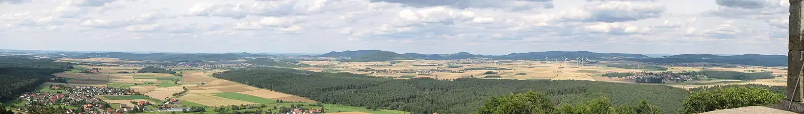 Nordostblick von der Weidelsburg: Links vorne der Ippinghäuser Grund mit Ippinghausen und dem tiefer gelegenen Weiler Leckringhausen, schräg rechts dahinter Wolfhagen und der Ofenberg (372,5&nbsp;m; 6,8&nbsp;km entfernt) rechts der Stadt und am Westrand des Altenhasunger Grabens; weiter rechts der Isthaberg (523,1&nbsp;m; 7,1&nbsp;km) und schließlich die Isthaebene mit Bründersen vor Istha vor Oelshausen (Mitte) und Altenstädt vor Balhorn (rechts), die zum Ippinghäuser Grund hin vom bewaldeten Rauenstein gerahmt wird. Hintere Reihe: Links hinter den Windkraftanlagen Stromberg (362,2&nbsp;m; 14,0&nbsp;km) und Heidelbeerenberg (398&nbsp;m; 13,3&nbsp;km), rechts dahinter der Desenberg (343,6&nbsp;m; 25,6&nbsp;km); links des Ofenbergs der Warteberg (419&nbsp;m; 9,8&nbsp;km), zwischen beiden der Escheberg (448,9&nbsp;m; 16,0&nbsp;km); in der Bildmitte, hinter dem Isthaberg, der Große Bärenberg (600,7&nbsp;m; 12,3&nbsp;km) mit Funk- und Aussichtsturm, weiter rechts der Dörnberg (578,7&nbsp;m; 16,7&nbsp;km); hinter den Windkraftanlagen schließlich der Hohe Habichtswald (614,8&nbsp;m; 15,1&nbsp;km) und rechts der Schwengeberg (556,7&nbsp;m; 14,0&nbsp;km). Für eine detailliertere Beschreibung siehe Weidelsberg#Aussicht![5]