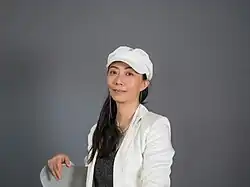 Portrait von Ying Wang vor grauem Hintergrund mit weißer Mütze