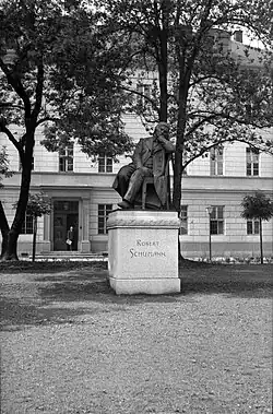 Denkmal auf einer Wiese, dahinter zwei kahle Bäume, dahinter ein Gebäude, Schwarz-weiß-Bild