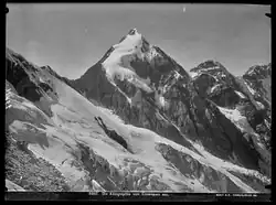 Schwarz-weiß Fotografie eines spitzen Berggipfels mit Schnee und Eismassen auf dunklem Fels