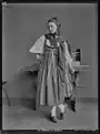 Junge Frau mit Tracht aus Basel-Landschaft steht vor einem Tisch, 1905